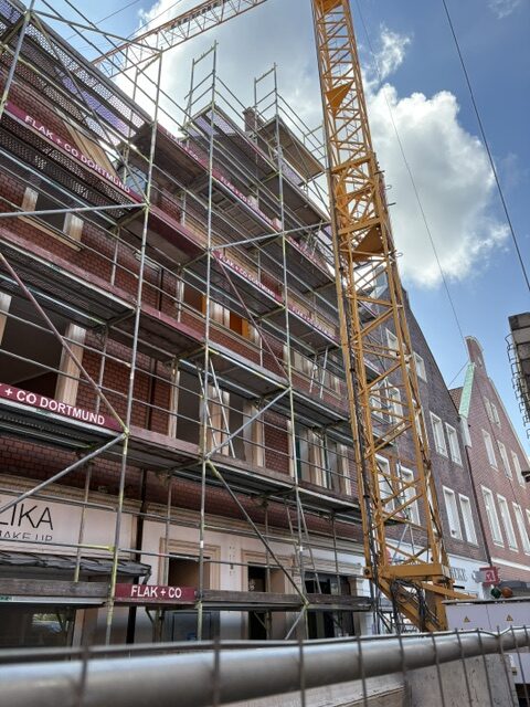 Fassade mit Baugeruest und gelbem Kran vor blauem Himmel, ohne Personen