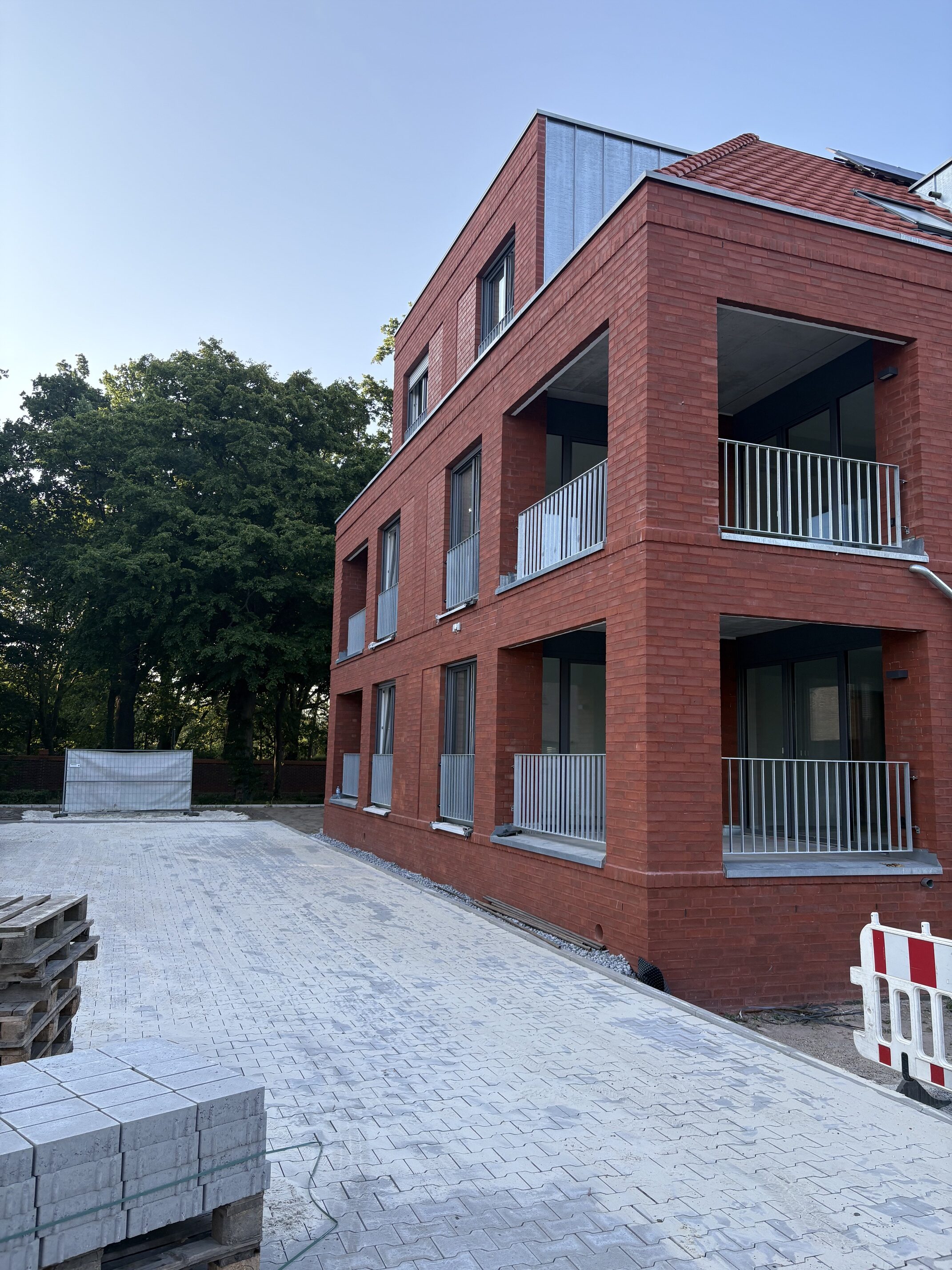 Rotes Mehrfamilienhaus mit Balkonen, ruhige Fassade, blauer Himmel