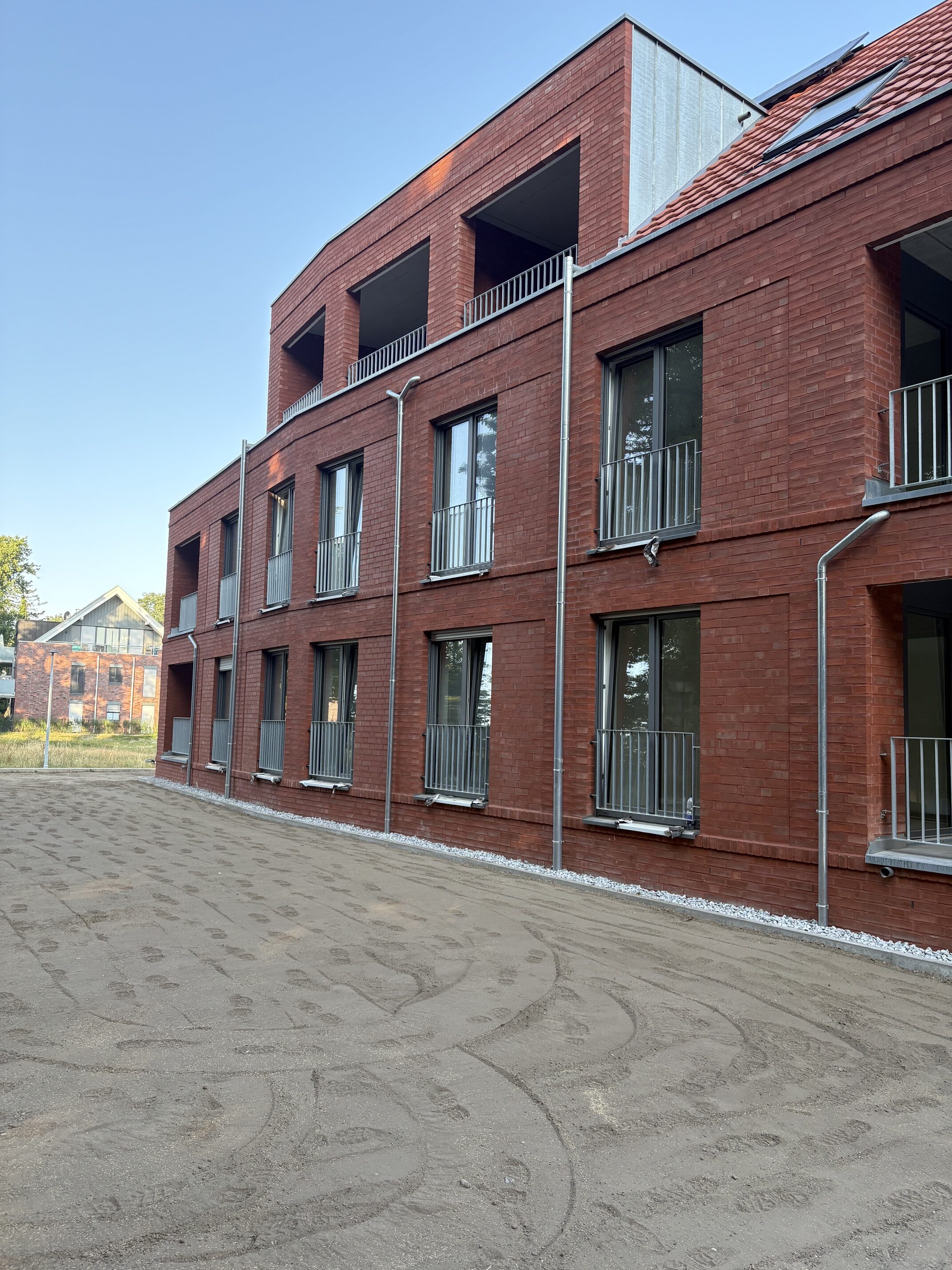 Modernes rotes Backsteingebaeude mit Balkonen und klaren Linien bei Sonne