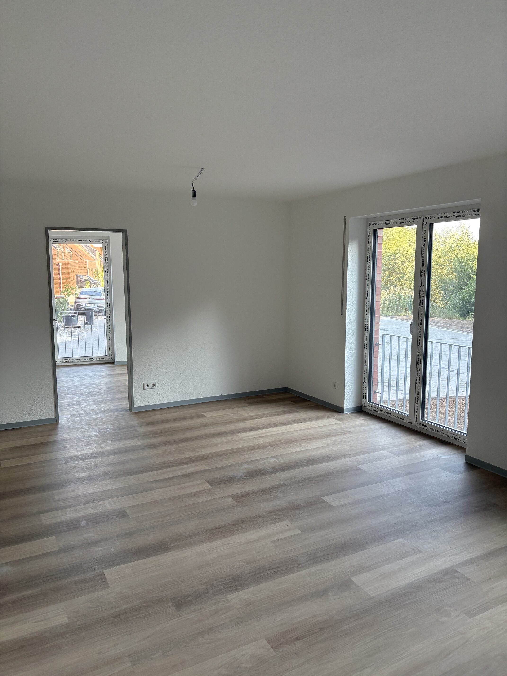 Leerer heller Raum mit Holzfußboden, großen Fenstern und Kabel an Decke