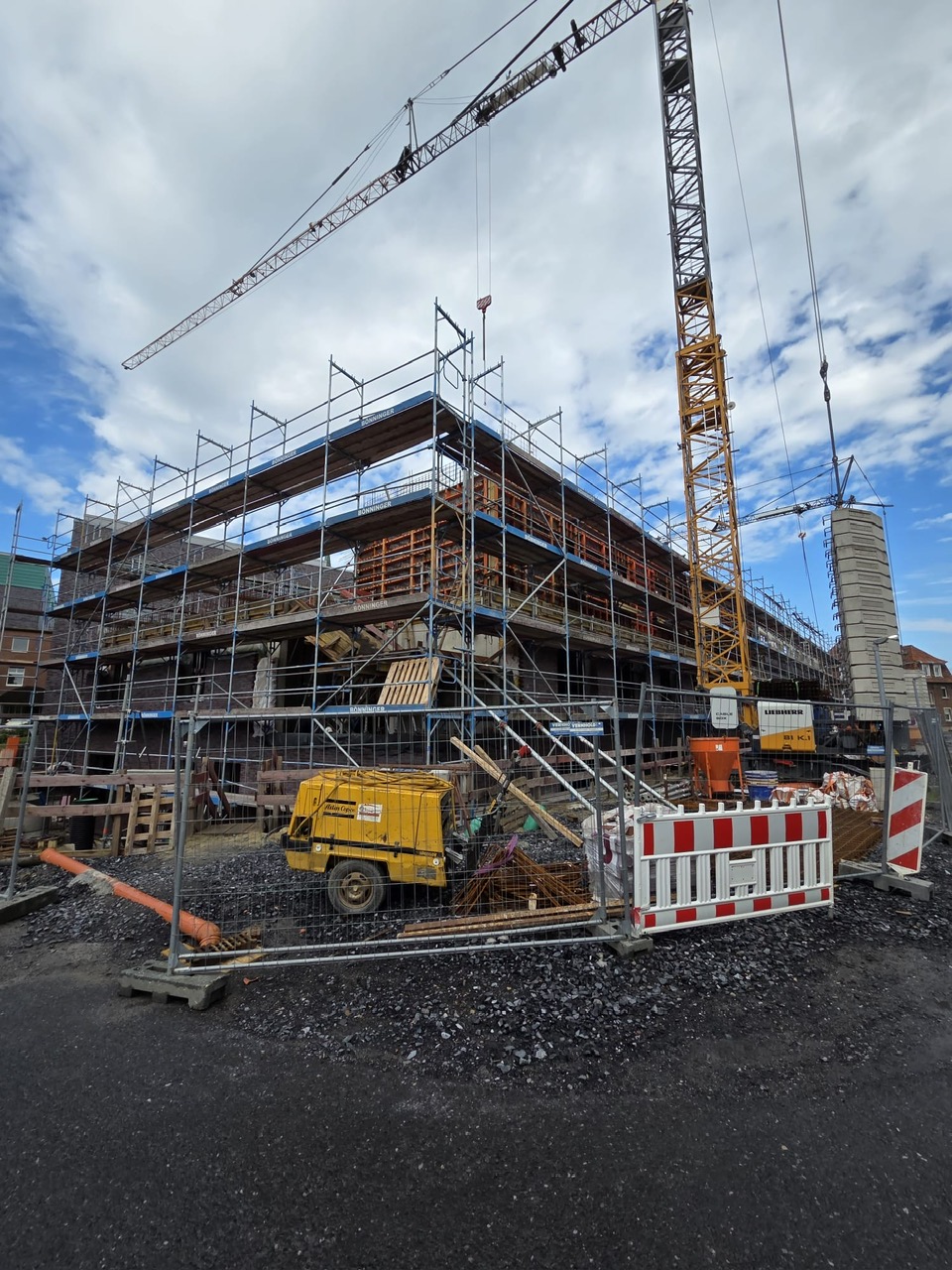 Baustelle mit Geruest und gelbem Kran unter wolkigem Himmel