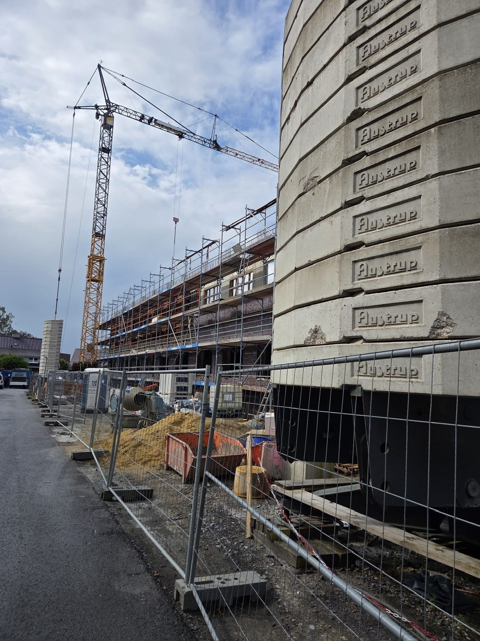 Grauer Baustellentank mit Betonrippen, Kran und Geruest unter Wolkenhimmel
